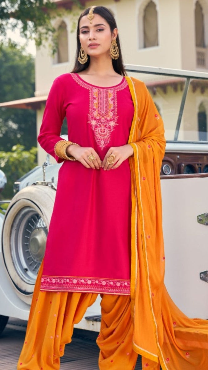 Woman in a pink and orange traditional outfit standing in front of vintage cars.